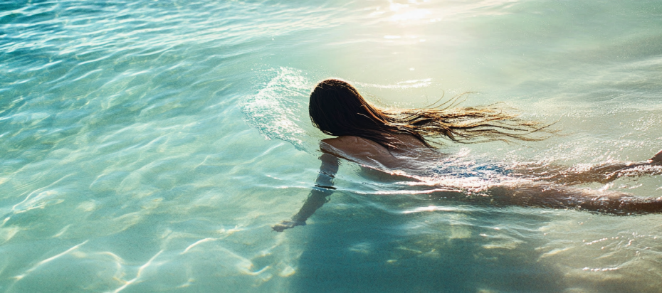 Can Salt Water Damage Your Hair Extensions? 4 Seamlessly blended hair extensions on a woman swimming in clear ocean water.