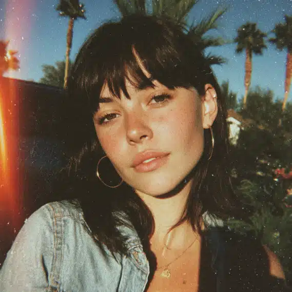 A 26-year-old woman with straight dark hair, taking a selfie outdoors with palm trees.